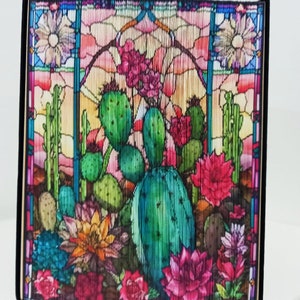 May include: A colourful, stained glass-style artwork depicting a cactus garden with pink, red, and yellow flowers. The artwork is framed in black and has a wood-like border.