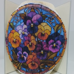 Può includere: Una scultura di arte libraria di un bouquet di violette viola, gialle e arancioni in una cornice in stile vetrata blu e bianca.