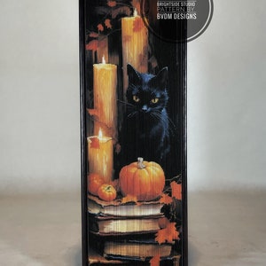May include: A black cat with yellow eyes sits in front of three lit candles and a pumpkin. The candles are in front of a stack of books. The image is framed with a dark wood border. The text "CRAFTED BY BRIGHT SIDE STUDIO PATTERN BY BVDM DESIGNS" is in a circle at the top right corner of the image.