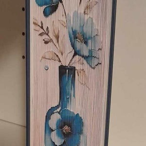Op de afbeelding: Een boekkunstwerk met blauwe bloemen in een blauwe vaas. De bloemen zijn gemaakt van gevouwen pagina's van een boek.