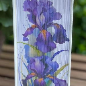 May include: A book with a purple and blue iris flower design on the cover. The book is made of folded paper and has a white background.