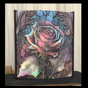 Peut inclure: Une rose colorée et irisée sur un fond sombre. La rose est entourée de feuilles et de vignes. L'image a une esthétique vintage et gothique.