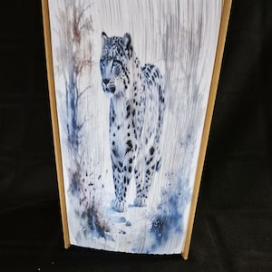Peut inclure: Sculpture décorative en forme de livre représentant un léopard des neiges aux yeux bleus dans une scène hivernale. L'œuvre est créée en éventail des pages d'un livre, avec les bords peints en or. Le léopard des neiges a des taches noires.