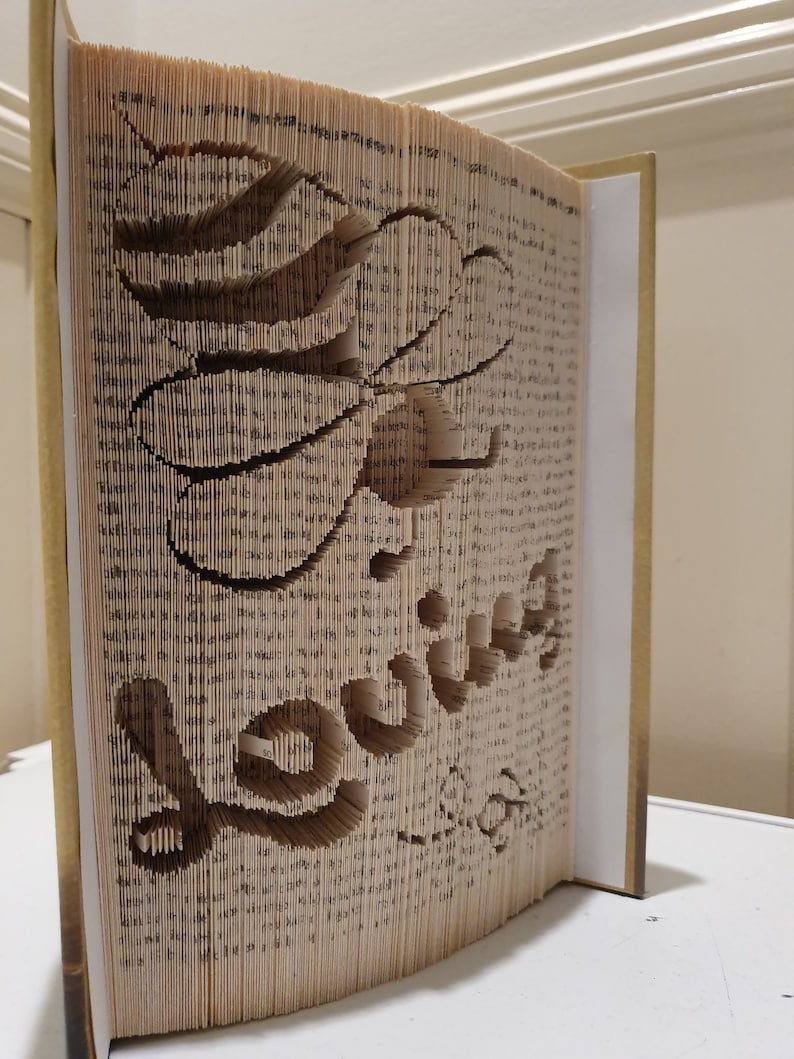 May include: A book with pages folded and cut to create a three-dimensional design of the word "love".