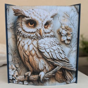 May include: A handcrafted book sculpture featuring a detailed owl design. The owl, with its intricate feather details and amber eyes, is perched on a branch. The book's pages are carefully folded to create a 3D effect, showcasing the owl against a backdrop of foliage.