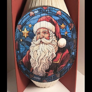 May include: A red, white, and blue book with a stained glass design of Santa Claus. The book is folded into a three-dimensional shape.