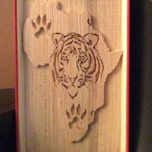 May include: A book art sculpture of the continent of Africa with a tiger's face and paw prints carved into the pages.
