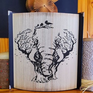 Pode incluir: Uma obra de arte de livro em preto e branco que representa um elefante feito com as páginas de um livro. O elefante é formado por duas árvores cujos ramos se entrelaçam para criar a cabeça e a tromba do elefante. O elefante está sobre um fundo branco.