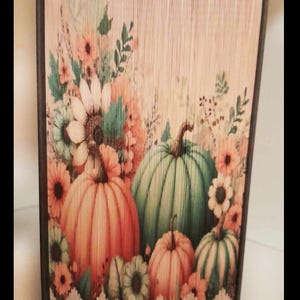 May include: A book art piece with a fall theme. The cover is decorated with a floral design and three pumpkins. The pumpkins are green, orange, and a lighter orange. The book is bound in a dark brown cover with a white lace trim.