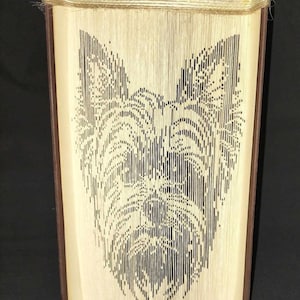 May include: A book art sculpture of a Yorkshire Terrier dog's face, made from the pages of a book, with a brown leather cover and a jute border.