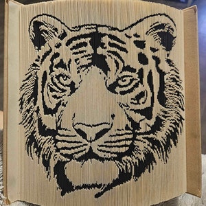 K&ouml;nnte beinhalten: Ein schwarzer und wei&szlig;er Papiertigerkopf, gefaltet aus den Seiten eines Buches. Das Gesicht des Tigers ist mit Streifen und Schnurrhaaren detailliert.
