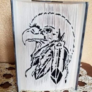 May include: A black and white book art sculpture of an eagle's head with feathers. The eagle's head is facing the right side of the image. The sculpture is made by folding the pages of a book.