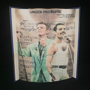 May include: A vintage-style print of David Bowie and Freddie Mercury, with the song title "Under Pressure" and the songwriters' names listed below. The image is printed on a textured background that resembles sheet music.