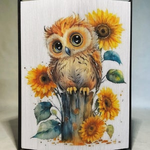 May include: A watercolor painting of a brown and orange owl perched on a wooden post with sunflowers behind it.