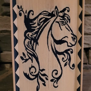 May include: A decorative wooden panel featuring a black horse head silhouette with flowing mane and floral accents. The panel has a natural wood tone with dark blue trim and a geometric border. The artwork is displayed on a stone surface.