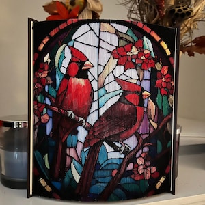 May include: A stained glass style wall decor featuring two red cardinals perched on a branch with red flowers. The background is a colorful mosaic of blue, green, and purple.