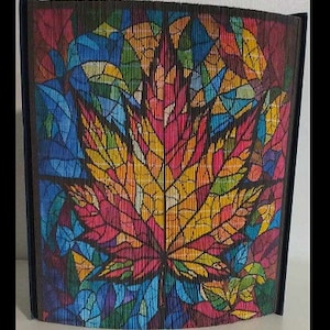 May include: A colorful stained glass style image of a maple leaf with red, yellow, orange, blue, and green hues. The leaf is framed in a black wood frame.