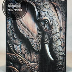 Peut inclure: Un gros plan sur une œuvre d'art murale décorative représentant un éléphant en détail, avec un design complexe. L'éléphant est rendu dans des tons de brun, d'or et de noir, avec un effet texturé, presque en 3D. L'œuvre d'art est encadrée d'une bordure noire.