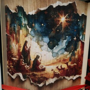 May include: A book art piece with a nativity scene image. The book is folded into a 3D shape and the image is visible through the folds. The image is of a night sky with a bright star and a nativity scene with Mary, Joseph, and the baby Jesus. The book is bound in brown leather and has a red ribbon.