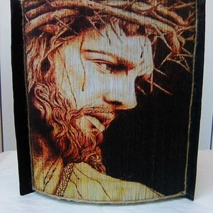 May include: A book art sculpture of Jesus Christ with a crown of thorns. The sculpture is made of folded pages of a book and is framed with a black border and a brown rope.