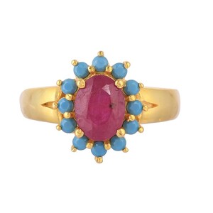 May include: A gold ring featuring a central oval-shaped red gemstone surrounded by a halo of twelve small, round, bright blue turquoise stones. The band is smooth and polished, with the cluster setting mounted directly onto the top of the ring.