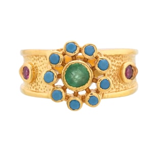 May include: Gold ring with a green gemstone surrounded by a circle of blue gemstones. Two red gemstones are on either side of the center stone.