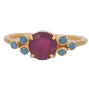 May include: A gold ring with a large, round, dark red gemstone surrounded by smaller, round, light blue gemstones.