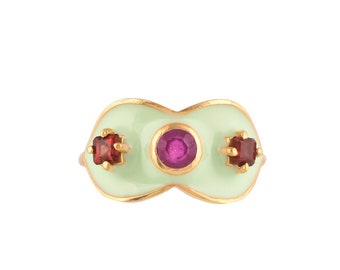 May include: A gold ring with a light green enamel setting. The ring has three gemstones: a large pink gemstone in the center and two smaller red gemstones on either side.