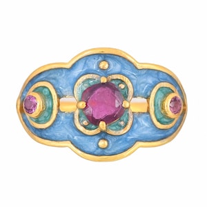 Puede incluir: Un anillo de oro con un diseño de esmalte azul y tres piedras preciosas rosas. El anillo tiene un motivo floral y un borde decorativo.