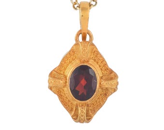 May include: A gold-colored pendant necklace featuring an oval, dark red gemstone set in an ornate, textured frame. The pendant hangs from a delicate gold chain, creating a classic and elegant jewelry piece.