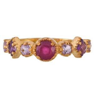 Op de afbeelding: Een gouden ring met een rode robijn-edelsteen en kleinere paarse edelstenen. De ring heeft een delicaat, versierd ontwerp.