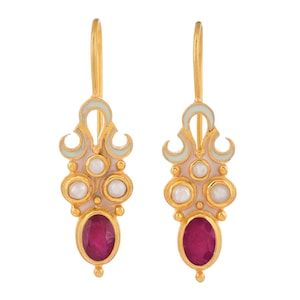 May include: A pair of gold-colored earrings with a light pink and pale green design. Each earring features three small white pearls and a large oval-shaped, deep red gemstone. The earrings have a decorative, ornate design.
