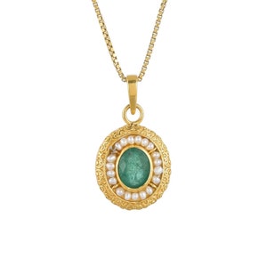 May include: A gold-colored pendant necklace featuring an oval, emerald-green gemstone surrounded by small, white pearls. The pendant has a decorative, filigree-style border and hangs from a delicate gold chain.