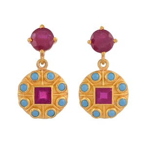 May include: A pair of gold-toned earrings. Each earring features a round, deep red gemstone at the top and a square, deep red gemstone at the center. The earrings are adorned with turquoise-colored gemstones and are set against a white background.