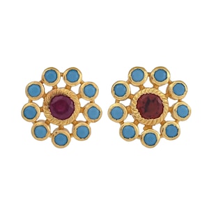 May include: A pair of gold earrings with a red gemstone surrounded by a circle of smaller blue gemstones.