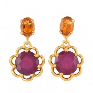 May include: Gold dangle earrings with a round, dark pink gemstone set in a flower-shaped frame and a smaller, oval, orange gemstone above.