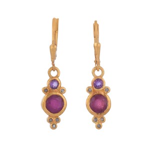 May include: Gold dangle earrings with a pink gemstone surrounded by smaller white gemstones and a purple gemstone above it.