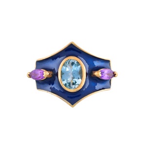May include: A gold ring with a blue enamel setting and a light blue oval gemstone. Two smaller purple gemstones are set on either side of the larger stone.