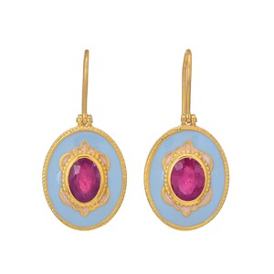 May include: A pair of gold-colored drop earrings. Each earring features a light blue oval with a pink and gold decorative border. A large, oval-shaped, ruby-colored stone is set in the center of each earring.