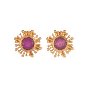 May include: A pair of gold earrings with a pink gemstone in the centre of each earring. The earrings are shaped like a sun with rays extending out from the centre.