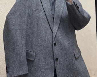 May include: A gray tweed blazer with a classic notched lapel and two front pockets. The blazer has a two-button closure and a tailored fit. The fabric has a subtle textured pattern. The blazer is worn over a gray turtleneck.