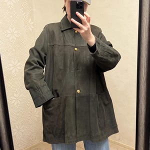Puede incluir: Chaqueta de ante verde oliva oscuro con botones dorados y dos bolsillos delanteros. La chaqueta tiene un cuello clásico y un corte entallado. El modelo lleva una gorra gris y vaqueros azules.
