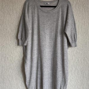 May include: A light gray, short-sleeved dress hanging on a black hanger. The dress has a round neckline and a slightly puffed sleeve design. The fabric appears to be a soft knit material. The brand name "acne" is visible on the neckline.