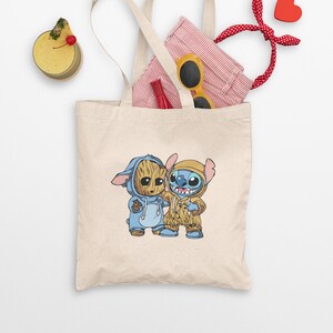 Pode incluir: Uma bolsa tote bege com uma imagem de desenho animado de Stitch e Groot usando pijamas combinando azul e amarelo. A bolsa está cheia de uma camisa listrada vermelha e branca, óculos de sol amarelos e um laço de cabelo vermelho.