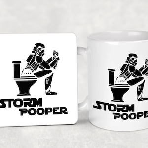 Può includere: Tazza e sottobicchiere in ceramica bianca con una silhouette nera di uno Stormtrooper seduto su un water. Il testo "Storm Pooper" è stampato sotto l'immagine.