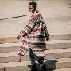 May include: A person wearing a long, striped, multi-colored coat with blue jeans and black boots. The person is walking down a set of stairs.