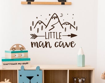 Op de afbeelding: Een bruine muursticker met een bergketen, sterren, een halve maan, een pijl en de tekst "LITTLE man cave".