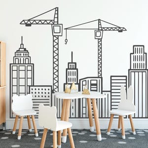 May include: A child's play area with a white table and three white chairs with bear and bunny ear designs. The wall features a black and white cityscape mural with construction cranes and buildings.