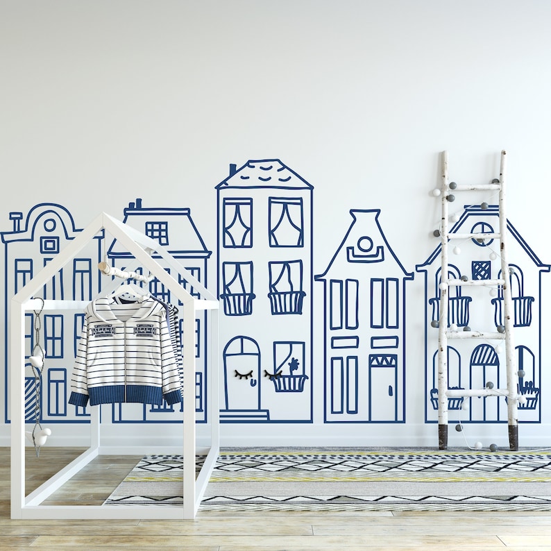 May include: A white wooden playhouse with a blue and white striped shirt hanging on a hanger inside. The playhouse is in front of a white wall with a blue hand-drawn cityscape design.