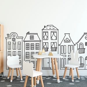 May include: A white playroom with a white wall featuring a black and white illustration of a row of houses. There are four white chairs with wooden legs and a small wooden table with a white top in the center of the room.